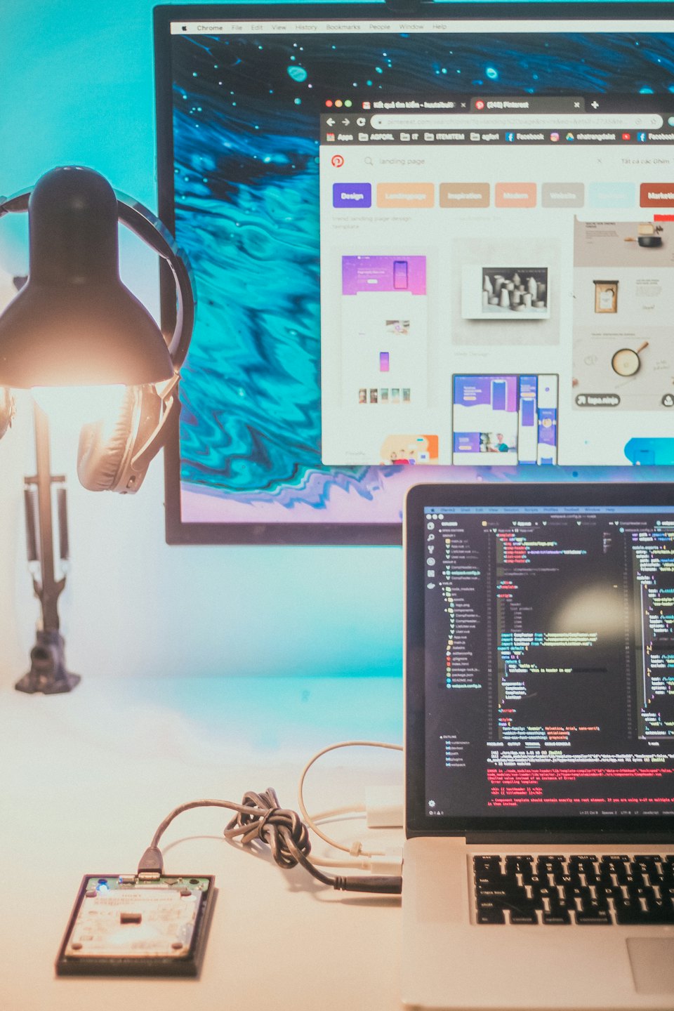 Laptop and monitor displaying programming code on a cluttered desk.